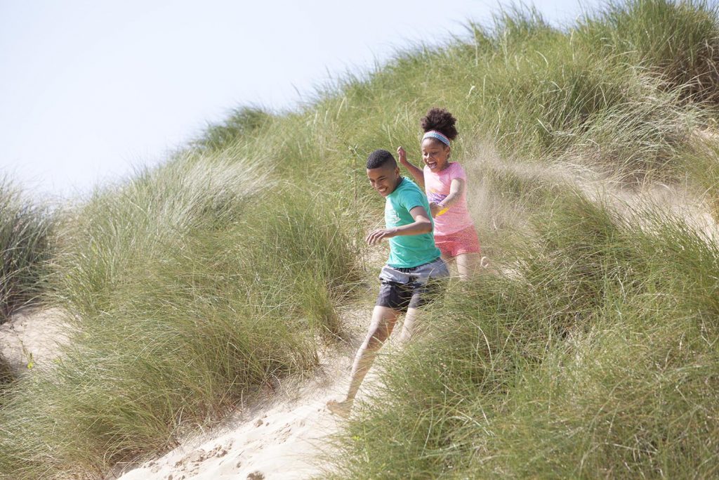 Two children playing on the sand dunes in Cornwall